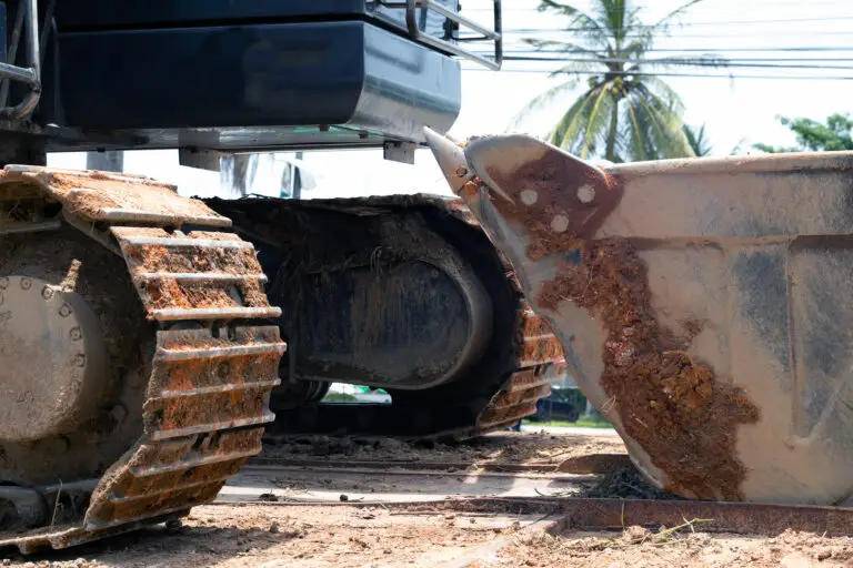 The importance of cleanliness in transportation - a dirty excavator has mud stuck in its tracks and bucket. Before loading, always rinse your work equipment.